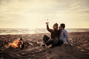 Image showing Young Couple Sitting On The Beach beside Campfire drinking beer