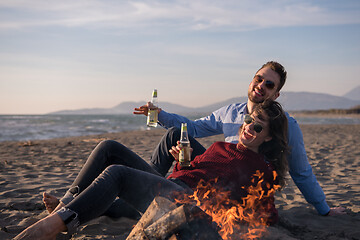 Image showing Young Couple Sitting On The Beach beside Campfire drinking beer