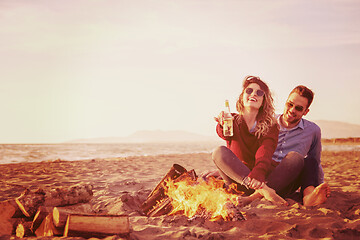 Image showing Young Couple Sitting On The Beach beside Campfire drinking beer