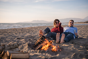 Image showing Young Couple Sitting On The Beach beside Campfire drinking beer