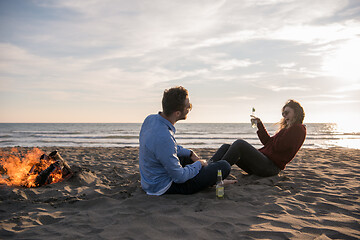 Image showing Young Couple Sitting On The Beach beside Campfire drinking beer