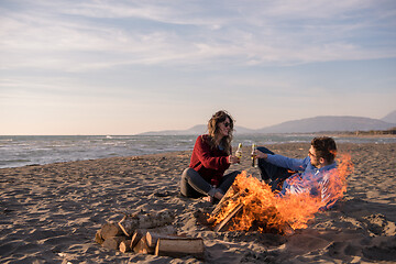 Image showing Young Couple Sitting On The Beach beside Campfire drinking beer