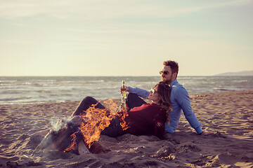 Image showing Young Couple Sitting On The Beach beside Campfire drinking beer