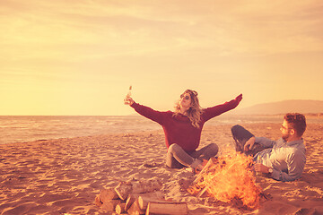 Image showing Young Couple Sitting On The Beach beside Campfire drinking beer