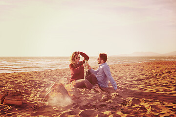 Image showing Young Couple Sitting On The Beach beside Campfire drinking beer