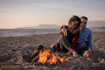 Image showing Young Couple Sitting On The Beach beside Campfire drinking beer