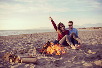 Image showing Young Couple Sitting On The Beach beside Campfire drinking beer