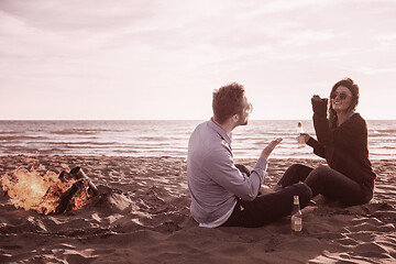 Image showing Young Couple Sitting On The Beach beside Campfire drinking beer