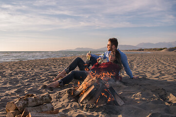 Image showing Young Couple Sitting On The Beach beside Campfire drinking beer