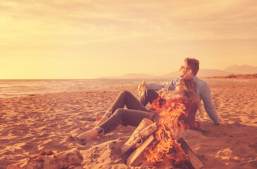 Image showing Young Couple Sitting On The Beach beside Campfire drinking beer