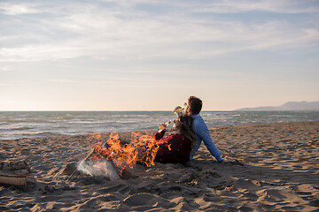 Image showing Young Couple Sitting On The Beach beside Campfire drinking beer