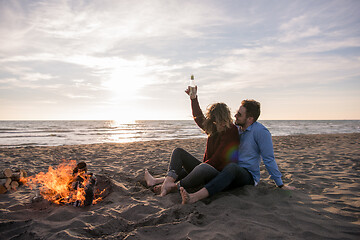 Image showing Young Couple Sitting On The Beach beside Campfire drinking beer