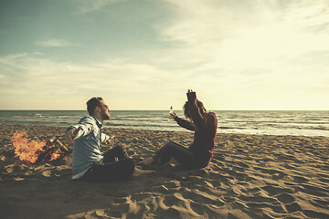 Image showing Young Couple Sitting On The Beach beside Campfire drinking beer