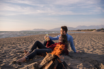 Image showing Young Couple Sitting On The Beach beside Campfire drinking beer