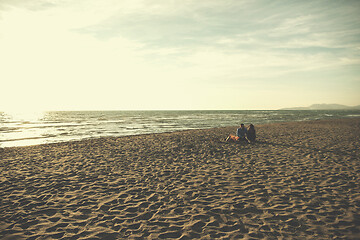 Image showing Young Couple Sitting On The Beach beside Campfire drinking beer