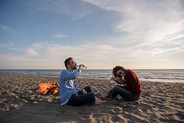 Image showing Young Couple Sitting On The Beach beside Campfire drinking beer