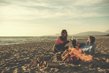 Image showing Young Couple Sitting On The Beach beside Campfire drinking beer