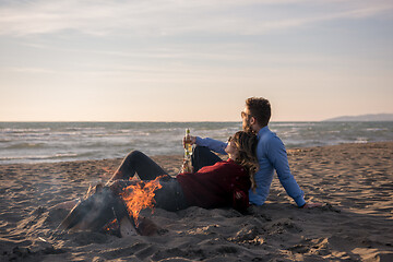 Image showing Young Couple Sitting On The Beach beside Campfire drinking beer