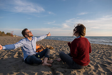 Image showing Young Couple Sitting On The Beach beside Campfire drinking beer