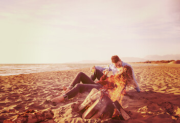 Image showing Young Couple Sitting On The Beach beside Campfire drinking beer