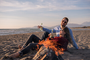 Image showing Young Couple Sitting On The Beach beside Campfire drinking beer