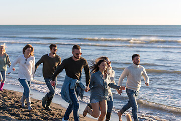 Image showing Group of friends running on beach during autumn day