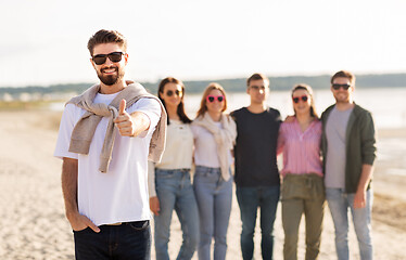 Image showing happy man with friends on beach showing thumbs up