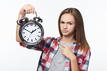 Image showing Unhappy teen girl holding big alarm clock pulling discontent face