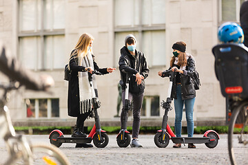 Image showing Trendy fashinable group of friends riding public rental electric scooters in urban city environment at fall. New eco-friendly modern public city transport in Ljubljana, Slovenia