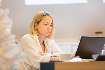 Image showing Young female entrepreneur wearing cosy warm bathrobe working remotly from home in winter Christmas time during 2020 corona virus pandemic. Work from home, selter in place, concept.