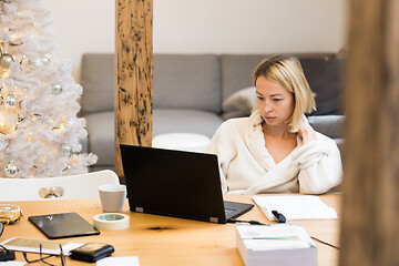 Image showing Young female entrepreneur wearing cosy warm bathrobe working remotly from home in winter Christmas time during 2020 corona virus pandemic. Work from home, selter in place, concept.