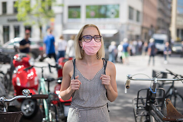 Image showing Portrait of casual yound woman walking on the street wearing protective mask as protection against covid-19 virus. Incidental people on the background