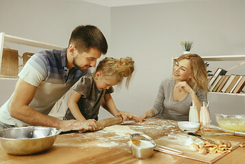 Image showing Cute little girl and her beautiful parents preparing the dough for the cake in kitchen at home