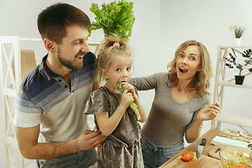 Image showing Cute little girl and her beautiful parents are cutting vegetables in kitchen at home