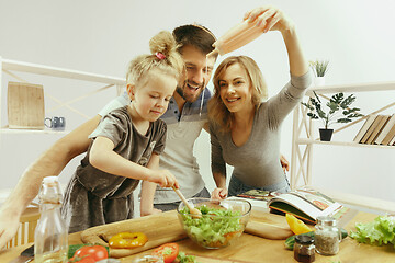 Image showing Cute little girl and her beautiful parents are cutting vegetables in kitchen at home