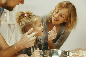 Image showing Cute little girl and her beautiful parents preparing the dough for the cake in kitchen at home