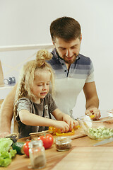 Image showing Cute little girl and her beautiful parents are cutting vegetables in kitchen at home