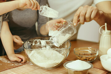 Image showing Cute little girl and her beautiful parents preparing the dough for the cake in kitchen at home