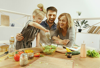 Image showing Cute little girl and her beautiful parents are cutting vegetables in kitchen at home