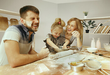 Image showing Cute little girl and her beautiful parents preparing the dough for the cake in kitchen at home