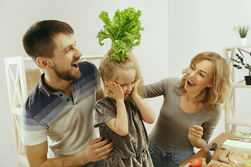 Image showing Cute little girl and her beautiful parents are cutting vegetables in kitchen at home