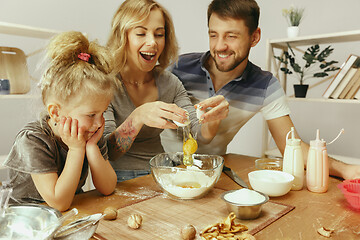 Image showing Cute little girl and her beautiful parents preparing the dough for the cake in kitchen at home