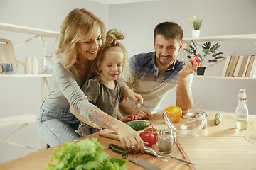 Image showing Cute little girl and her beautiful parents are cutting vegetables in kitchen at home