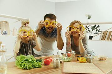 Image showing Cute little girl and her beautiful parents are cutting vegetables in kitchen at home