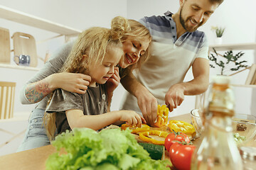 Image showing Cute little girl and her beautiful parents are cutting vegetables in kitchen at home