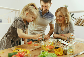 Image showing Cute little girl and her beautiful parents are cutting vegetables in kitchen at home