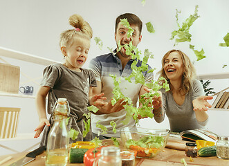 Image showing Cute little girl and her beautiful parents are cutting vegetables in kitchen at home