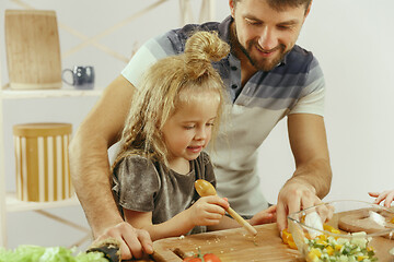 Image showing Cute little girl and her beautiful parents are cutting vegetables in kitchen at home