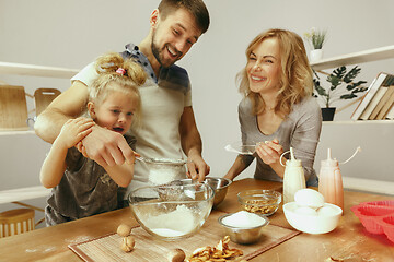 Image showing Cute little girl and her beautiful parents preparing the dough for the cake in kitchen at home