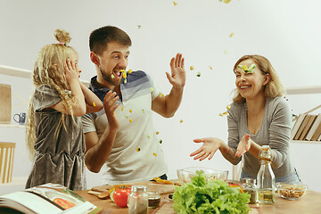 Image showing Cute little girl and her beautiful parents are cutting vegetables in kitchen at home